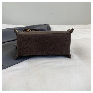 Detail view of the deep brown leather bag bottom with protective corners and gold hardware
