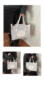 Detail view of white tote bag with repeating M pattern and central embossed emblem