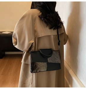 Detail einer schwarzen Patchwork-Clutch mit Schlangenmuster kombiniert mit einem Khaki-Mantel