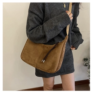 Detail of a brown suede hobo bag with a long tassel zipper and wide shoulder strap