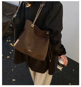 Detail of a brown suede tote bag with golden metal chains and drawstring side accents