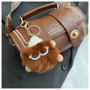 Brown fluffy monster keychain with mini knit hat on a vintage leather boston bag