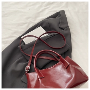 Détail d'un sac cabas bordeaux avec boucles en métal argenté sur un fond blanc doux