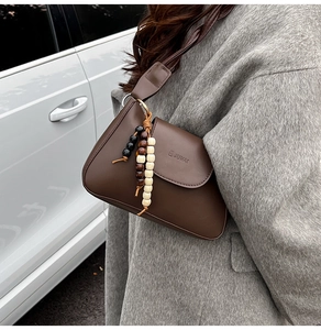 Close-up of a vintage brown leather underarm bag with a unique beaded tassel charm