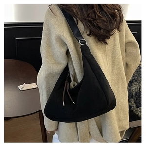 Detail of black suede crescent bag with brown drawstrings shown on a beige wool coat