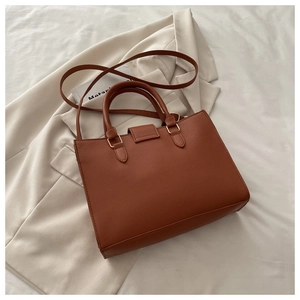 Close-up of brown litchi pattern tote bag with golden hardware on white blazer
