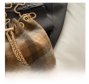 Macro detail of plaid wool bucket bag featuring golden chain and pearl drawstring charms
