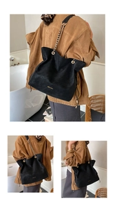 Detail of black leather tote bag featuring gold chain strap and side drawstring closure