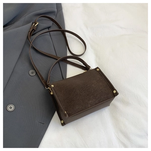 Detail of dark brown matte texture bag with gold hardware and shoulder strap on a grey suit
