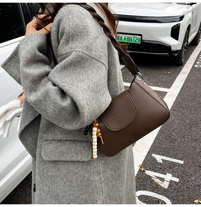 Close-up of deep brown leather underarm bag with woven strap and colorful bead tassel