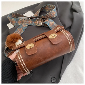 Detail of brown cylinder bag with gold rivets, ethnic strap and fur charm
