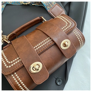 Detail of vintage brown textured handbag with gold rivets and ethnic style woven strap
