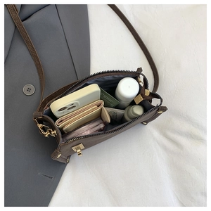 Detail showing inner capacity of brown crossbody bag with gold hardware and items inside