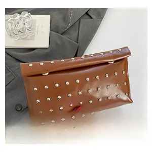 Detailed view of a brown leather clutch bag with silver studs held against a grey suit