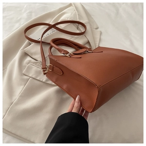 Nahaufnahme der braunen Handtasche aus Leder mit goldener Hardware auf beigem Blazer