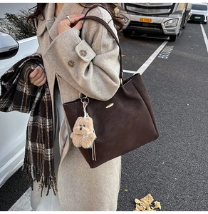 Detail of deep brown faux suede tote bag featuring a cute plush puppy charm and metal logo