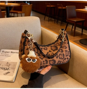 Close-up of leopard print crescent bag with plush pom-pom and gold chain detail