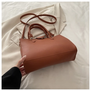 Detail of brown litchi grain leather handbag with dual handles and adjustable shoulder strap