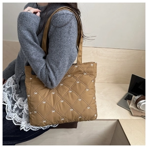 Dettaglio borsa shopper marrone trapuntata con ricami a fiocco bianchi e tracolla imbottita