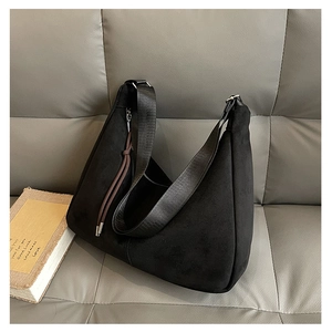 Detail of black suede hobo bag on sofa with wide shoulder strap and brown tassels