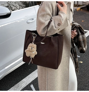 Brown suede tote bag with plush bear charm styled in outdoor casual street photography