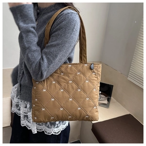 Dettaglio ravvicinato della borsa trapuntata marrone con ricami di fiocchi bianchi e texture