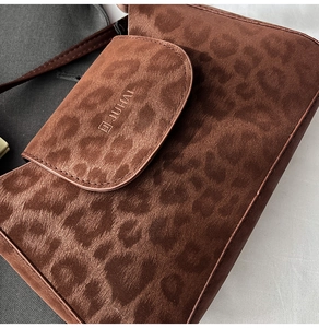 Detail shot of leopard print texture and brand logo on a brown suede underarm bag