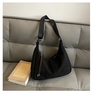Detail of a large black matte hobo bag with a wide strap and tassel on a sofa