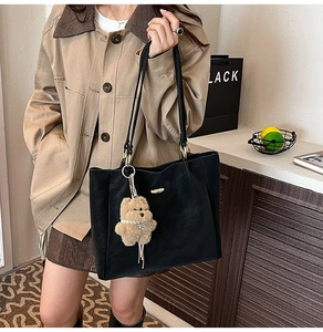Model wearing a black leather tote bag with a brown plush bear charm for daily commute