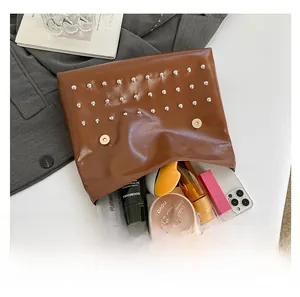 Macro view of brown leather rivet clutch showing spacious interior with cosmetics