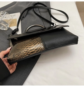 Detail der schwarzen Handtasche aus Leder mit Schlangenhaut-Muster und Metallring-Griff