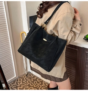 Detail view of large black tote bag with matte finish and gold metal accents on model