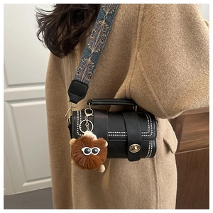 Detail of black leather cylinder bag with bohemian strap and plush monster charm