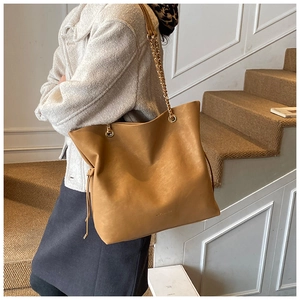 Detail of caramel leather tote bag showing gold chain strap and drawstring side detail