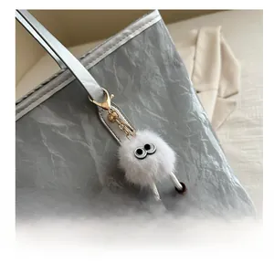 Close-up of a white plush ball bag charm with big eyes and brown shoes on a silver tote bag