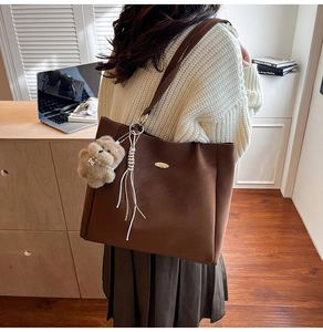 Detail view of a large brown leather tote bag with bear pendant worn by a model in casual style