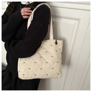 Dettaglio di fiocchi ricamati su borsa tote trapuntata a rombi color bianco crema