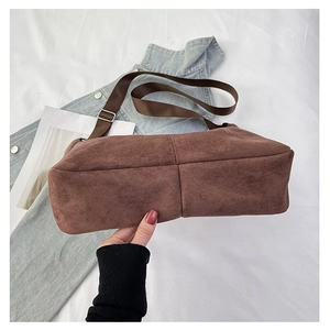 Detail of reinforced bottom stitching and wide adjustable strap on brown suede tote bag