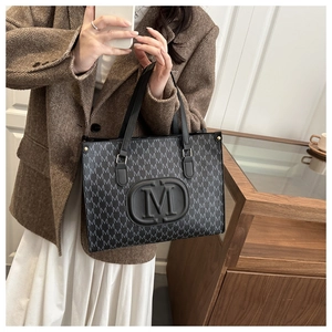 Detail of a large black tote bag with letter M prints and a central embossed logo detail