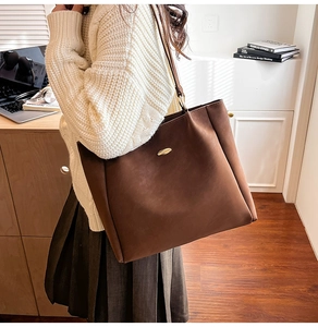 Detail of a large brown tote bag with gold metal plaque shown in a stylish commute setting