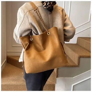 Detail of caramel faux leather bucket bag with gold chain strap and drawstring closure