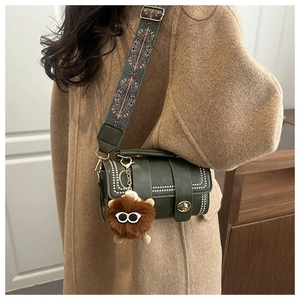 Detail of dark green leather cylinder bag with wide woven strap and plush charm