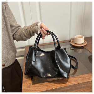 Détail d'un sac cabas noir brillant avec doubles poignées et bandoulière sur une table