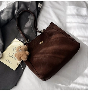 Detail of coffee brown tote bag with gold emblem, plush bear charm and leather texture
