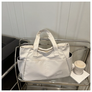 Detail of a creamy white nylon tote bag with fashion label and side pocket functionality