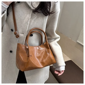 Brown patent leather bucket bag with adjustable strap worn with a beige winter coat