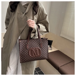 Detail of retro brown tote bag featuring all-over M letter pattern and embossed center logo