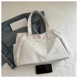 Top-down view of white nylon tote bag with front pockets and fashion text patch detail
