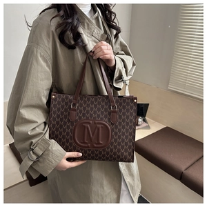 Detail of vintage brown tote bag with M-letter monogram print and leather handle
