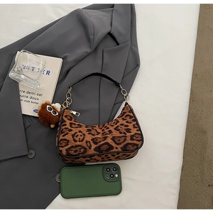 Detailed view of leopard print shoulder bag with gold chain and plush charm next to phone